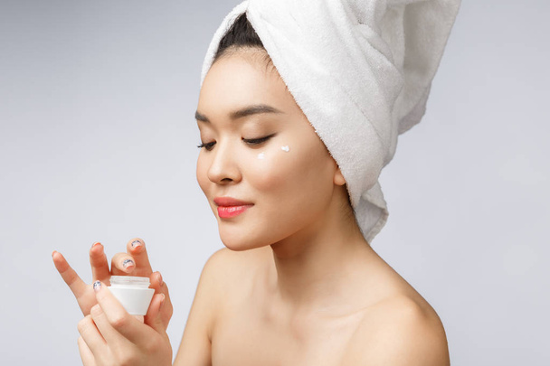 Gesundheits- und Schönheitskonzept - Attraktive asiatische Frau cremt ihre Haut ein, isoliert auf weiß - Foto, Bild