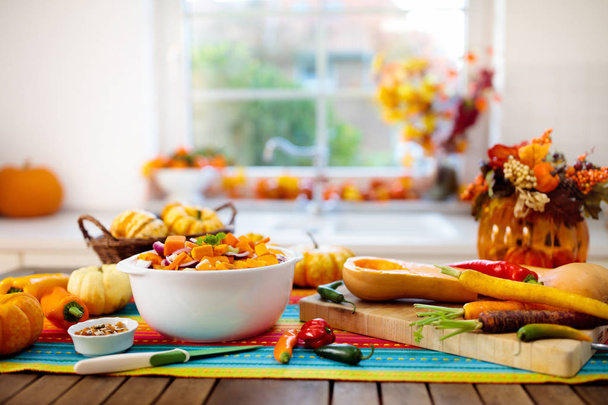 Κολοκύθα, κρεμμύδι και καρότο έτοιμα για μαγείρεμα σούπας για το φθινοπωρινό γεύμα. Υγιή φθινοπωρινά λαχανικά για αποκριάτικο γεύμα. Κομμένο σε ξύλινο τραπέζι στην ηλιόλουστη κουζίνα. - Φωτογραφία, εικόνα