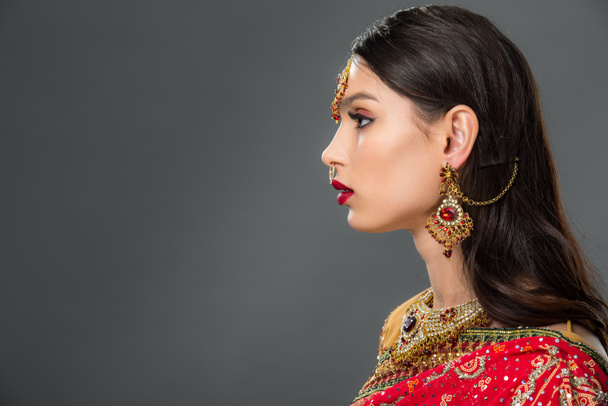 side view of attractive indian woman posing in traditional sari and bindi, isolated on grey  - Photo, Image