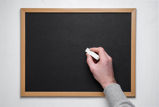 Hand holding chalk on blackboard. Male hand with chalk on the empty blackboard or chalkboard. - Photo, Image