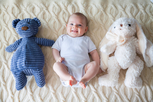 smiling adorable baby girl lying on her back with rabbit and bear toys - Foto, Imagem