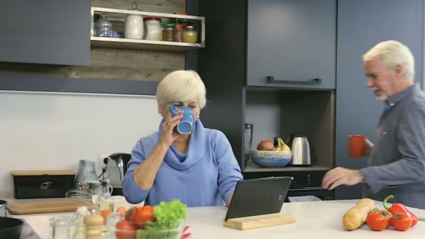 Old aged couple at the kitchen. Looking recipe (or watching news) at the gigital tablet. - Video, Çekim