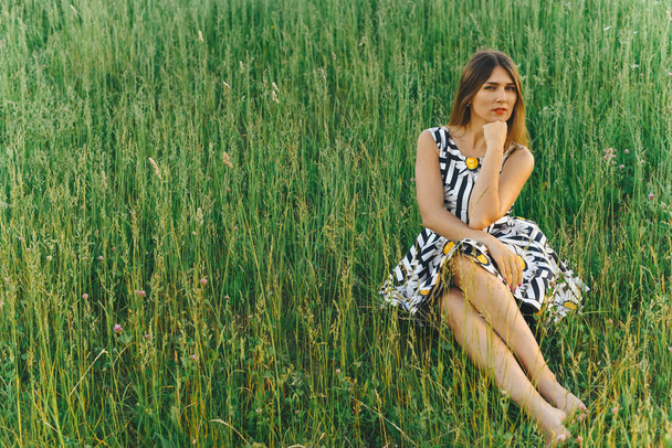 Nuori nainen mekko istuu vihreä ruoho
 - Valokuva, kuva