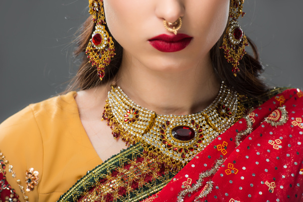 обрезанный вид индийской женщины, позирующей в традиционном сари и ювелирных украшениях, изолированных на сером
  - Фото, изображение