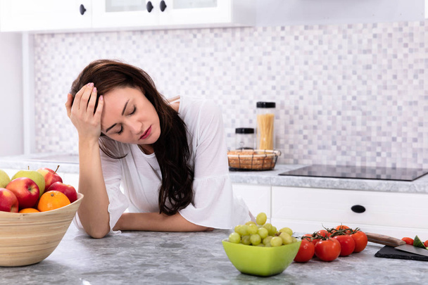 Fresh Fruits In Front Of Upset Young Woman Leaning On Kitchen Counter - Fotó, kép