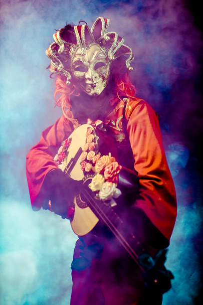 carnival man in venetian costume and mask posing with guitar against misty background - Fotó, kép