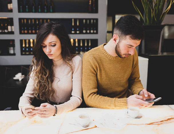 Jeune couple au bar tout en utilisant un téléphone portable. Les réseaux sociaux dans la vie réelle peuvent avoir des effets négatifs
. - Photo, image