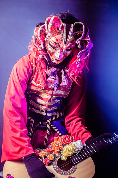 man in venetian costume and mask posing with guitar against dark background - Foto, imagen
