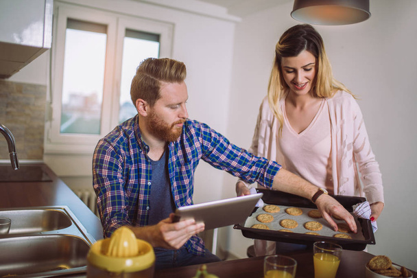 Hermosa pareja joven está utilizando una tableta digital y sonriendo mientras cocina en la cocina en casa
 - Foto, imagen