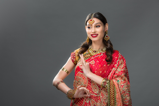 улыбающаяся индианка в сари и аксессуарах с гьянской мудрой, изолированная на сером
  - Фото, изображение