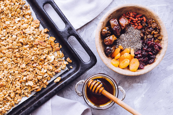 Preparation process of homemade roasted granola on baking sheet with agave nectar and dried fruit and berries to add. Superfood. Healthy eating concept. Top view. Flat lay. - Photo, image