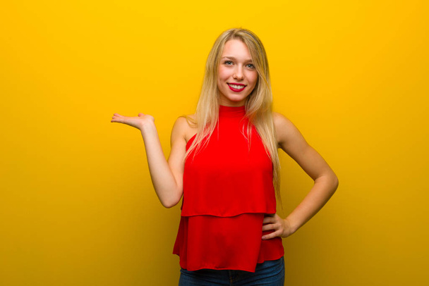 Jeune fille avec robe rouge sur le mur jaune tenant copyspace imaginaire sur la paume pour insérer une annonce
 - Photo, image