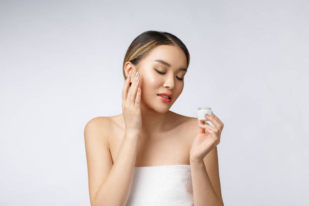 Mulher asiática aplicando creme cosmético na pele no fundo branco isolado
 - Foto, Imagem
