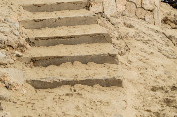 Крупный план каменных лестниц и песка на средиземноморском пляже, следы на песке. - Фото, изображение