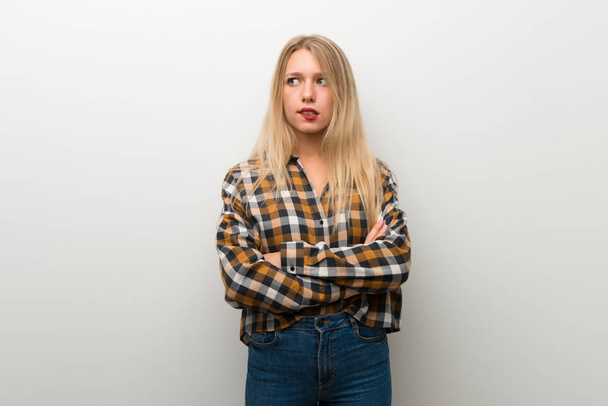 Blonde young girl over white wall with confuse face expression while bites lip - Fotoğraf, Görsel
