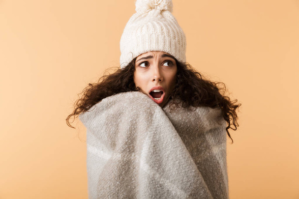 Upset young woman wearing winter scarf standing isolated over beige background, shivering - Photo, image