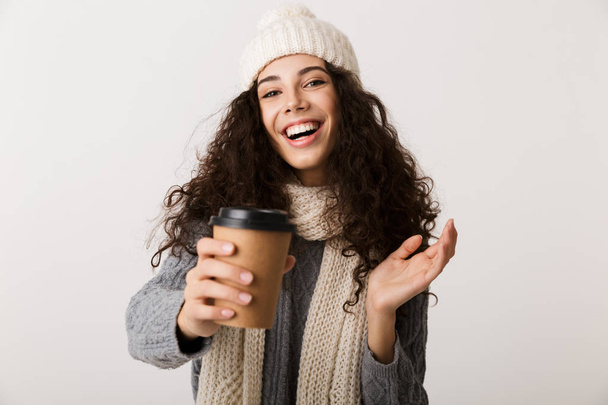 Cheerful young woman wearing winter scarf standing isolated over white background, holding takeaway cup of coffee - Φωτογραφία, εικόνα
