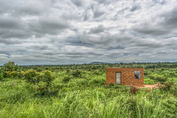 Вид на традиционный терракотовый дом, изолированный посередине на фоне пейзажа, на фоне облачного неба, в Анголе
 - Фото, изображение