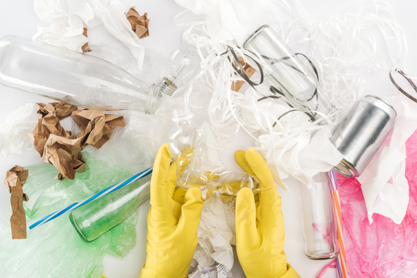 Cropped view of man holding empty plastic bottle among can, glass bottles, plastic bags, paper strips, paper and plastic tubes - Photo, Image