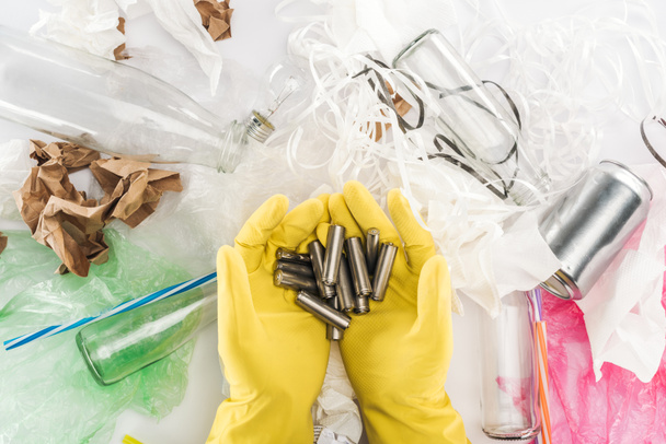 Cropped view of man holding batteries among can, glass bottles, plastic bags, paper strips, paper and plastic tubes - Photo, Image