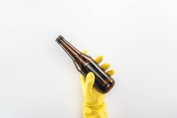 Cropped view of man in yellow rubber gloves holding empty glass bottle on grey background  - 写真・画像