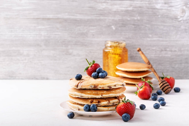 Blueberry pancakes served with strawberries and blueberries over white background. Copy space - Foto, Bild