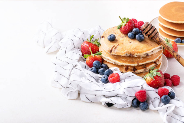 Blueberry pancakes served with strawberries, blueberries, raspberries, honey and maple syrup over white background - Zdjęcie, obraz