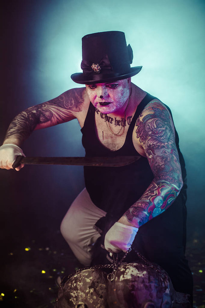 portrait of zombie killer wearing hat with machete and zombie heads posing against dark background - 写真・画像