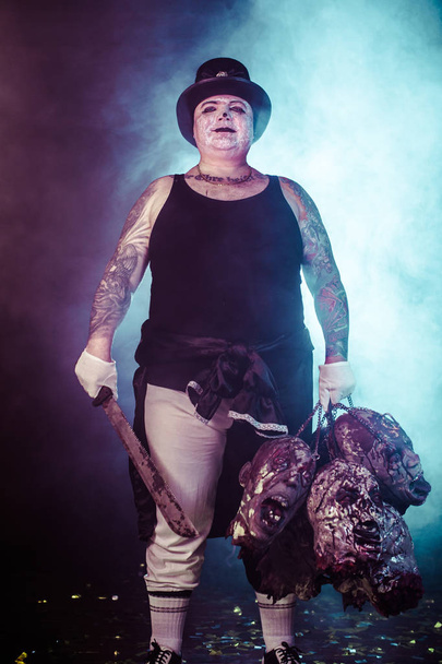 retrato de asesino zombi usando sombrero con machete y cabezas de zombi posando sobre fondo oscuro
 - Foto, imagen