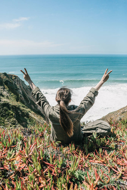 Turysta dziewczyna siedzi na wzgórzu i podnosi ręce, pokazując, jak ona jest. - Zdjęcie, obraz