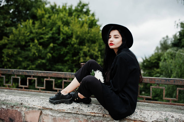 Sensual girl all in black, red lips and hat. Goth dramatic woman hold white chrysanthemum flower. - Zdjęcie, obraz