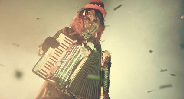 festival man in venetian costume and mask posing with accordion against misty background - Foto, Imagen