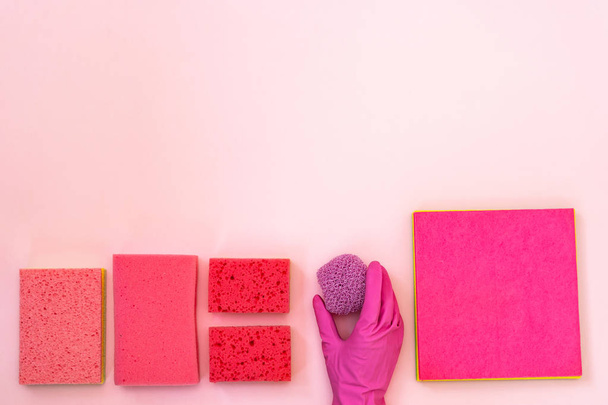 Hand holding scrub near pink polyurethane dish sponges for washing. They laying isolated on pastel background with empty space for text - Foto, Imagen