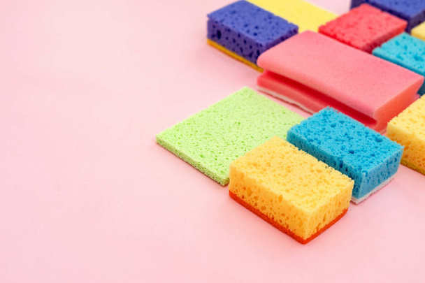 Algumas esponjas coloridas de poliuretano e outras coisas de limpeza isoladas em fundo rosa pastel com espaço vazio para texto
 - Foto, Imagem