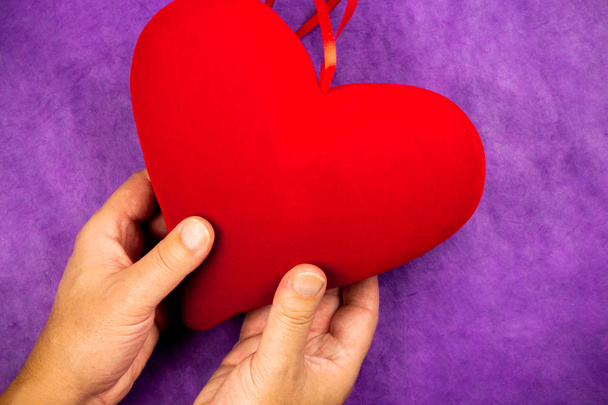 man's hand holding a big red heart on purple background - Foto, imagen