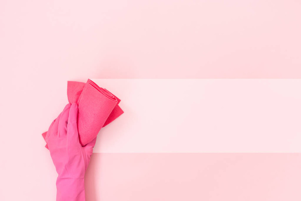 Mujer con guantes de látex sosteniendo toalla de limpieza en la mano aislada sobre fondo rosa pastel con espacio vacío para texto
 - Foto, imagen