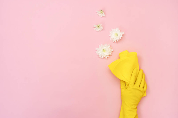 Woman in rubber gloves holding yellow cleaning towel in her hand with small flowers around, isolated on pastel pink background with empty space for text - Photo, Image