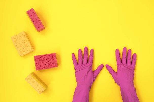 Mujer sosteniendo dos manos en guantes de goma rosa cerca de una esponja de lavado aislada sobre fondo amarillo
 - Foto, imagen