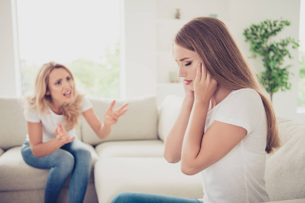 Close up photo two people mum and teenager daughter yelling fighting try not listen hide ears sick tired of depression wear white t-shirts jeans in bright flat sit on comfortable sofa  - Φωτογραφία, εικόνα