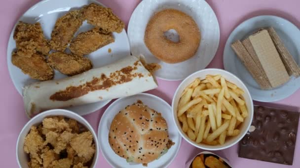 Unhealthy food concept. Fast food, burger, donut, french fries on a pink background. Hands taking food - Felvétel, videó