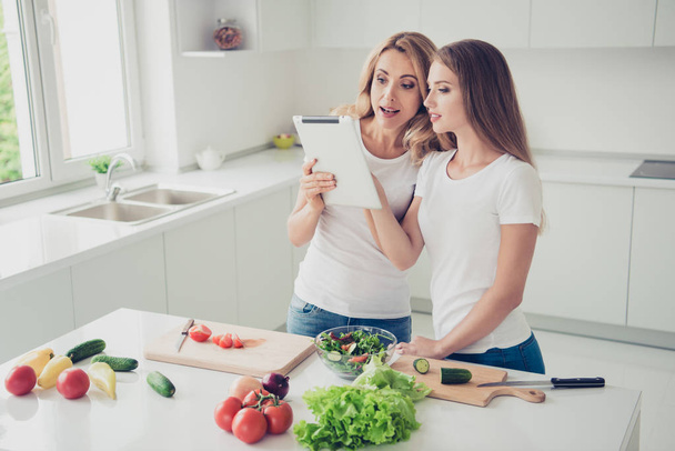 Two nice cute lovely sweet attractive charming cheerful people blonde mom mum cooking good vegan vegs food in modern light white interior room - Photo, image