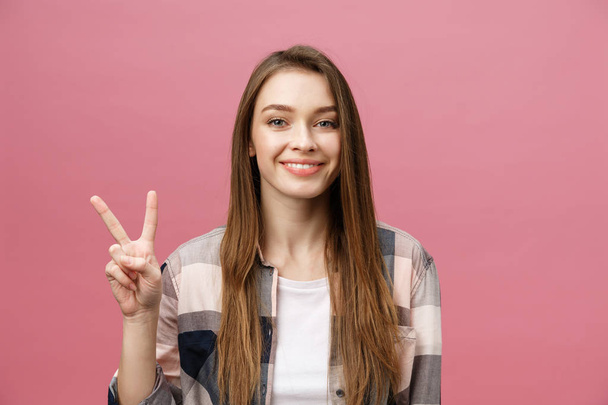 junge kaukasische Frau vor isoliertem Hintergrund, die lächelnd in die Kamera blickt und Finger zeigt, die Siegeszeichen machen. Nummer zwei - Foto, Bild