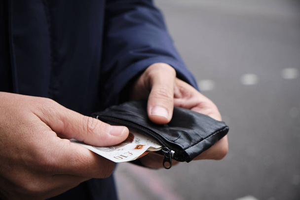 Nahaufnahme eines jungen kaukasischen Mannes auf der Straße, der ein paar Pfund Sterling-Banknoten aus seinem Portemonnaie zieht - Foto, Bild