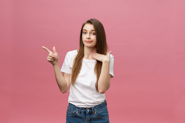Closeup of serious strict young woman wears white shirt looks stressed and pointing up with finger isolated over pink background - Photo, Image