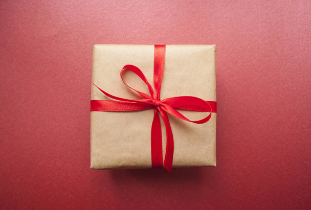 Pudełko na prezent związany z czerwoną wstążką na pastelowy różowy tło. - Zdjęcie, obraz