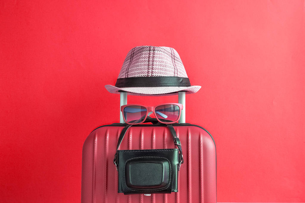 Suitcase with hat and retro camera on red background. Travel equipment minimal creative concept. - 写真・画像