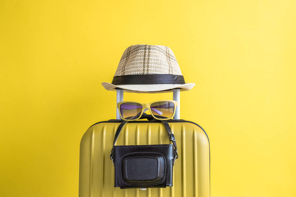 Suitcase with hat and retro camera on yellow background. Travel equipment minimal creative concept. - Foto, immagini