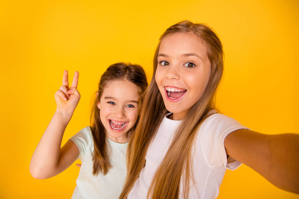 Self-portrait of nice-looking cute attractive lovely pretty cheerful cheery positive pre-teen girls showing v-sign isolated over bright vivid shine yellow background - Fotografie, Obrázek