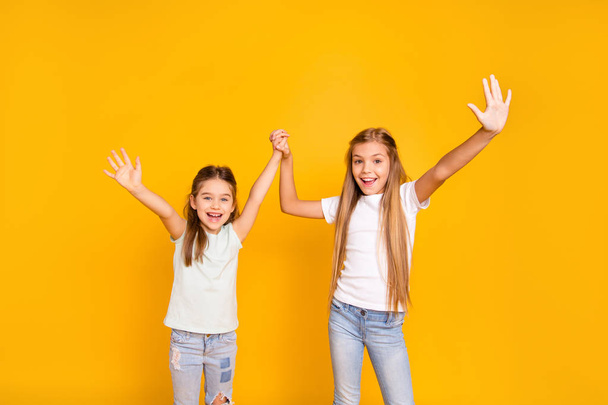 Portrait of two nice cool crazy attractive lovely cheerful cheery positive girlish girls holding hands having fun isolated over bright vivid shine yellow background - 写真・画像