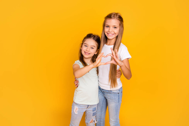 Portrait of two nice adorable stylish trendy attractive lovely sweet cheerful cheery positive caucasian pre-teen girls showing health healthy heart isolated over bright vivid shine yellow background - Foto, Imagen